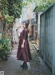 A woman in a maroon dress standing in an alleyway.