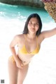 A woman in a yellow bikini standing on the beach.