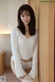 a woman in a white sweater and panties leaning against a wall