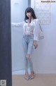 A woman standing in front of a mirror wearing ripped jeans and a white shirt.