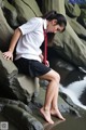 A woman in a school uniform sitting on a rock by the water.