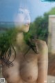 A naked woman standing in front of a window.