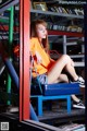 A woman sitting on a blue chair in front of a book shelf.