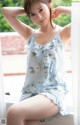 A woman sitting on a window sill wearing a blue floral dress.