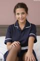 A woman in a blue uniform sitting on a bed.