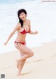 A woman in a red bikini running on the beach.